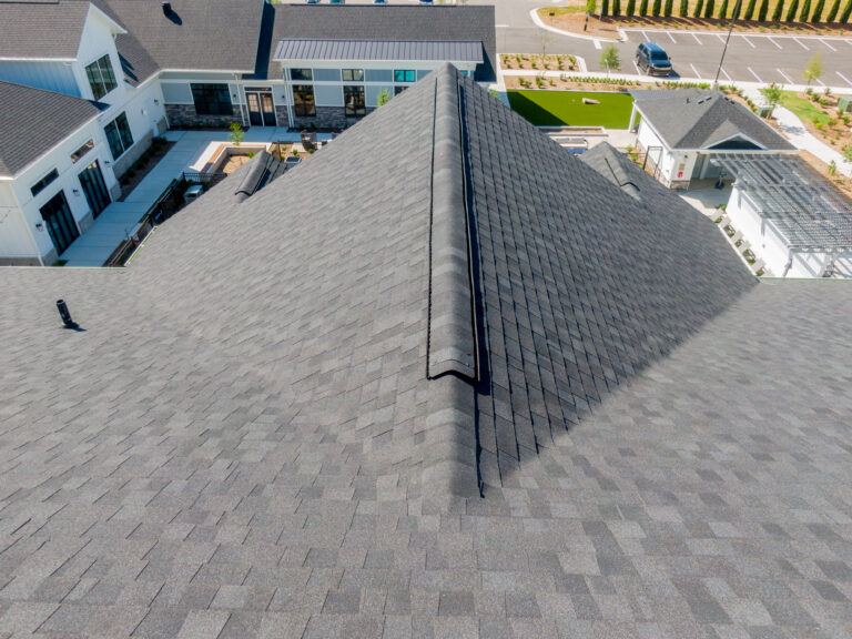 ridge vents A two-story house with brick and white siding, surrounded by grass, shrubs, and tall trees with bare branches, seen from above on a clear day. Aerial view of a gray shingle roof on a modern building, showing the peak and surrounding landscaped area, sidewalks, and parking lot.